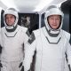 NASA astronauts Bob Behnken and Doug Hurley in their SpaceX spacesuits walking down a white corridor.
