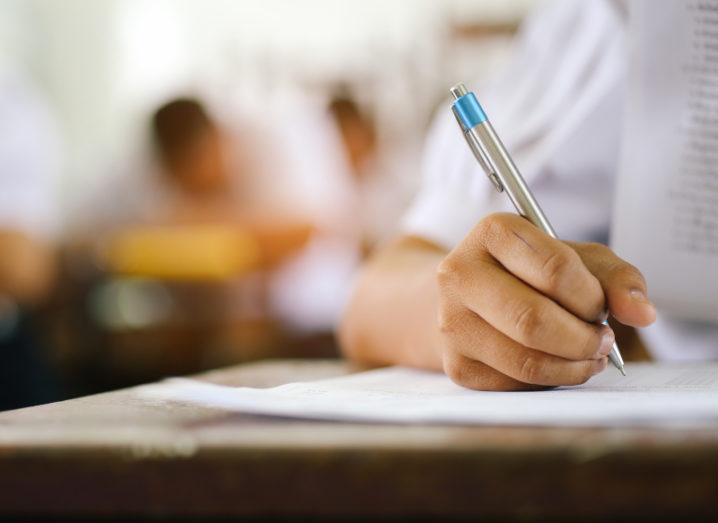 Close-up image of student in a uniform taking a test, writing answers on a piece of paper.