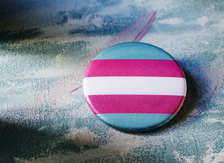 A badge bearing the trans pride flag of light blue, light pink and white stripes.