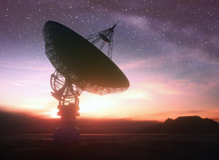Huge satellite antenna dish searching for radio signals in space at sunset.