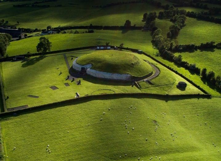 Aerial view of Newgrange, a circular structure covered in grass, blending into the fields around it.