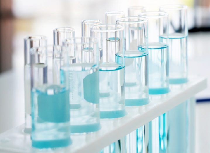 A line of test tubes in a test tube holder sitting on a table, all with blue liquid in them, representing life sciences.