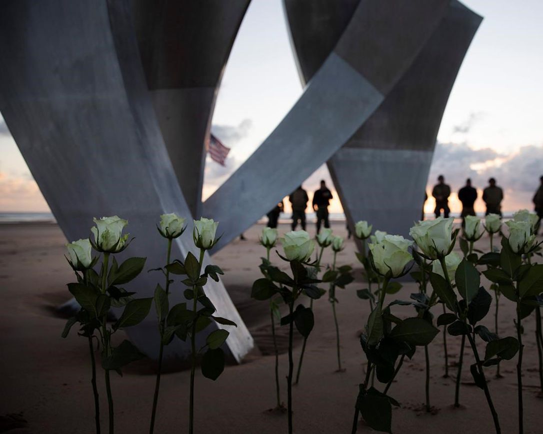 Men in a vintage US WWII uniforms stand behind flowers left at Les Braves monument after a D-Day 76th anniversary ceremony in Saint Laurent sur Mer, Normandy, France, Saturday, June 6, 2020. Due to coronavirus measures many ceremonies and memorials have been cancelled in the region with the exception of very small gatherings.