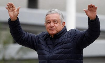 In this April 3, 2020 file photo, Mexican President Andres Manuel Lopez Obrador waves to supporters cheering from over an outside wall, after visiting a Mexican Social Security Institute (IMSS) hospital that will be converted to receive COVID-19 patients in the Coyoacan district of Mexico City.