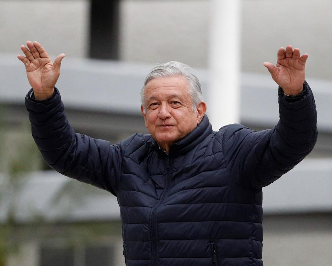 In this April 3, 2020 file photo, Mexican President Andres Manuel Lopez Obrador waves to supporters cheering from over an outside wall, after visiting a Mexican Social Security Institute (IMSS) hospital that will be converted to receive COVID-19 patients in the Coyoacan district of Mexico City.