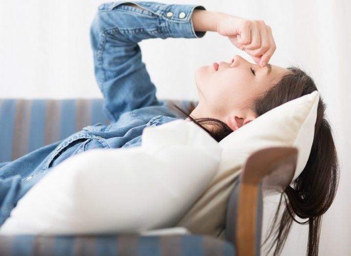 Fatigued woman holding the bridge of her nose while lying down on a couch.