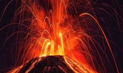 An erupting volcano spewing bright red lava at night.