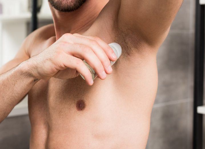 Cropped view of a man applying roll-on deodorant to his armpit.