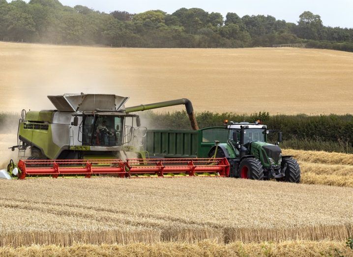 A combine harvester working in a field of wheat beside a tractor.