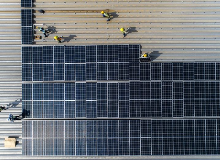 Bird’s-eye view of solar panels being installed on a large factory roof.