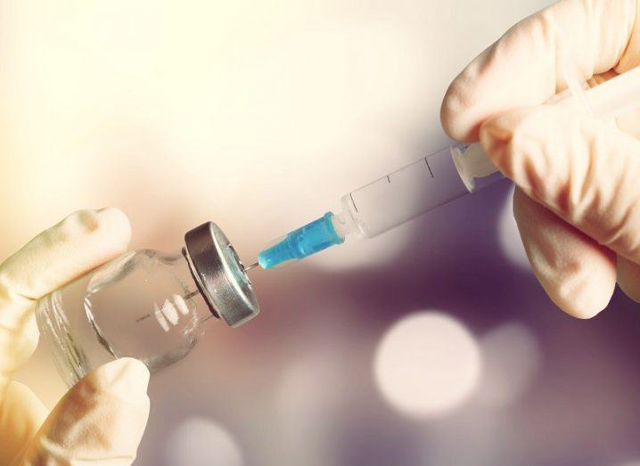 Gloved hands filling a syringe with a vaccine from a vial.