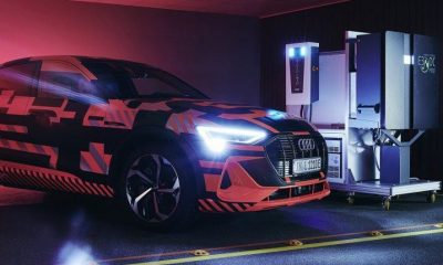An Audi E-tron car coloured black and neon red, with its lights on beside a bidirectional charging station.