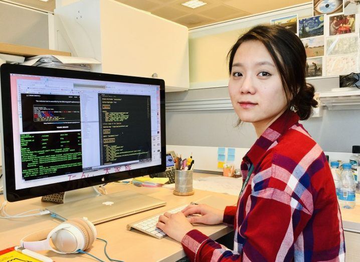 Jisun An in a tartan shirt turned to the camera while working at a desktop screen in her lab.