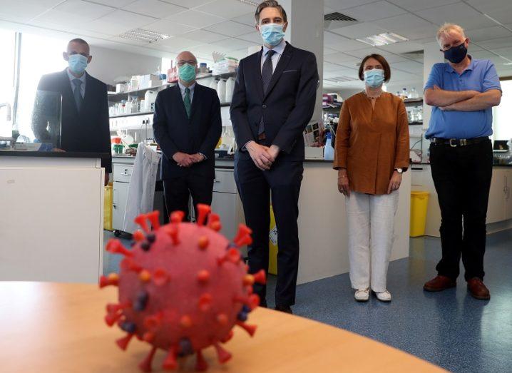 Kingston Mills, Mark Ferguson, Simon Harris, Aideen Long and Luke O’Neill wearing face masks and standing behind a model of the coronavirus.